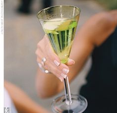 a woman holding a martini glass filled with cucumber