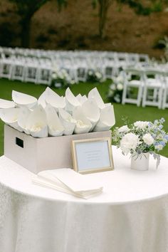 a white table topped with a box filled with flowers next to an empty photo frame