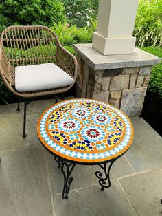 two chairs and a table on a patio with a stone pillar in the back ground