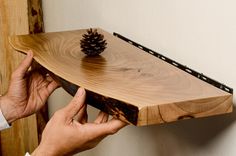 a person holding a wooden shelf with a pine cone on it and another hand reaching for the top