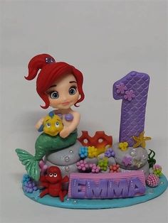 a little mermaid figurine sitting on top of a rock with the number one