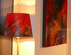 a lamp is next to two paintings on the wall and one has a red lampshade