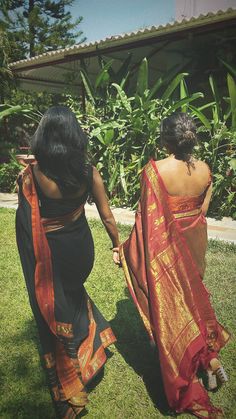 two women in sari walking on grass holding hands and looking off into the distance