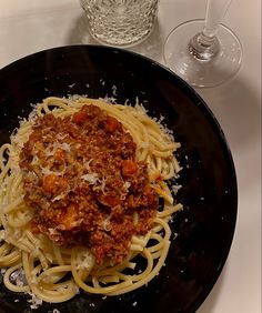 a black plate topped with spaghetti and sauce next to a glass of wine on a table