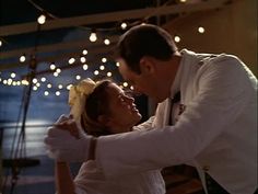 a man and woman dance together in front of string lights