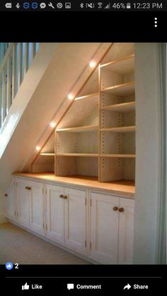 an atticed room with white cupboards and shelves in the wall, under a stair case