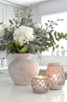 a white vase filled with flowers on top of a counter next to two lit candles