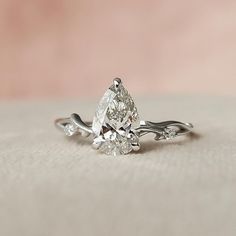 a pear shaped diamond engagement ring on a white cloth with a pink back droplet