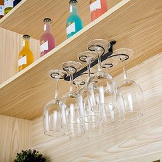 wine glasses and bottles are hanging from the ceiling in front of a shelf with wooden shelves