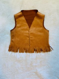 a tan leather vest with fringes on the front and back, sitting on a white background