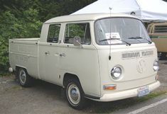 an old vw bus parked in a parking lot next to a tent and trees