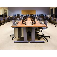 an empty room with multiple computers on the desks and chairs around it in front of a large screen