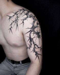 a man with barbed wire tattoo on his arm and shoulder, standing in front of a black background