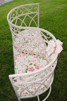 a white chair sitting in the grass on top of a green field with pink flowers