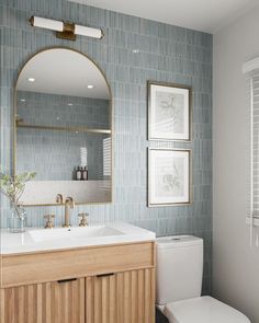 a white toilet sitting under a bathroom mirror next to a wooden sink vanity with two framed pictures on the wall