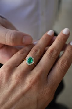 a woman's hand holding an emerald and diamond ring