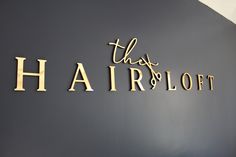 there is a sign that says this hair loft in gold letters on the wall above it