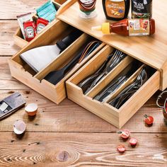 an open drawer on top of a wooden table filled with utensils and sauces