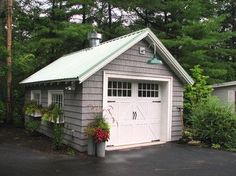 a gray garage with a green roof and white trim on the door is shown in front of some trees