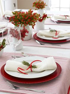 the table is set with red and white plates, napkins and place settings for christmas dinner