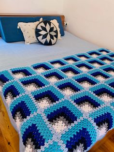 a blue and white crocheted blanket sitting on top of a bed next to pillows