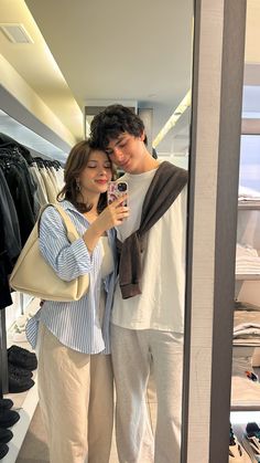 a man and woman taking a selfie in front of a closet full of clothes