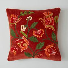 a red pillow with flowers and leaves embroidered on the front, sitting against a white wall