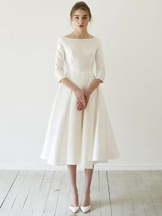 a woman wearing a white dress standing in front of a wall with her hands on her hips