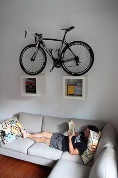 a man laying on top of a white couch under a bike mounted to the wall