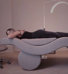 a woman laying on top of a white couch next to an office chair and lamp