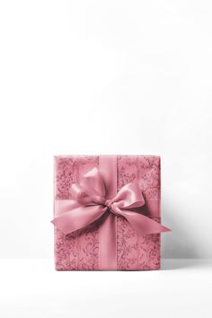 a pink gift box with a large bow on the front and side, sitting against a white background