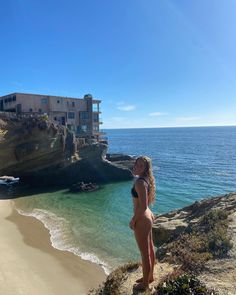 a woman standing on top of a cliff next to the ocean with a building in the background