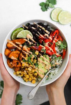 two hands holding a bowl filled with mexican food and garnished with cilantro