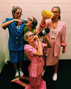 three women in pink dresses are drinking from wine bottles and one woman is holding a yellow cup