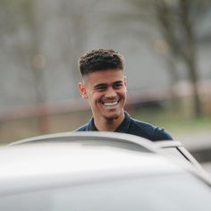 a smiling man standing next to a parked car