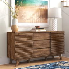 a wooden dresser sitting in front of a painting on the wall next to a lamp