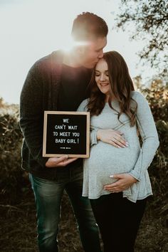 a pregnant couple kissing while holding a sign