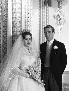 a man and woman standing next to each other in front of a wall wearing wedding dresses