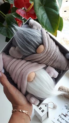 a hand holding a small stuffed animal in a box next to a potted plant