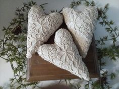 three decorative white heart shaped pillows sitting on top of a wooden box filled with pine needles