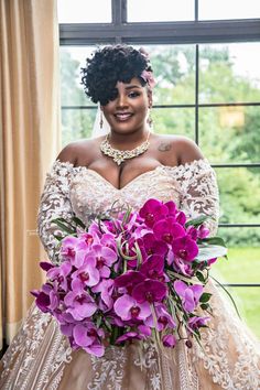 a woman in a wedding dress holding a bouquet of purple flowers and smiling at the camera