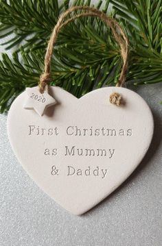 a personalised ceramic heart ornament hanging from a christmas tree with the words'first christmas as mummy & daddy '