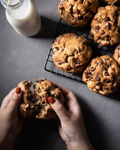 a person holding a chocolate chip cookie next to some milk