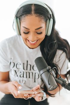 a woman wearing headphones is looking at her cell phone while sitting in front of a microphone