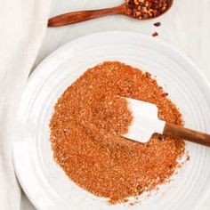 a white plate topped with spices next to a wooden spoon on top of a table