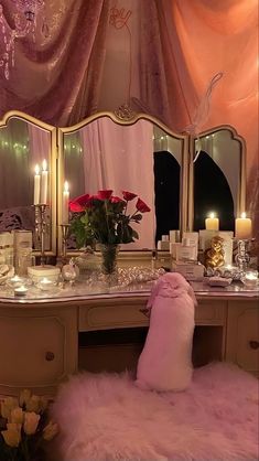 a vanity with candles and flowers on it in front of a pink curtained window