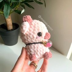 a hand holding a small pink crocheted teddy bear