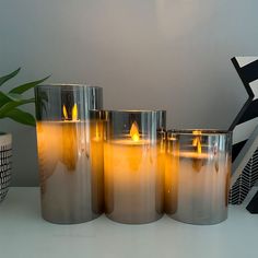 four lit candles sitting on top of a white table next to a potted plant