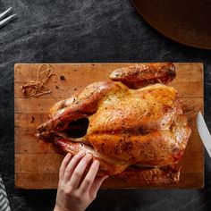 a person cutting up a turkey on top of a wooden cutting board with knifes