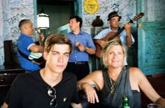 a group of people sitting around each other in front of a wall with guitars on it